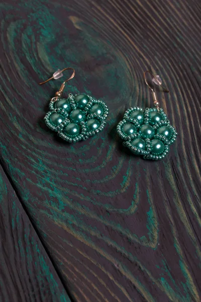 Homemade green earrings from beads. On brushed pine boards painted in black and green. — ストック写真