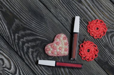 Knitted pink earrings and a bead brooch. Makeup kit. On brushed pine boards painted in black and white.