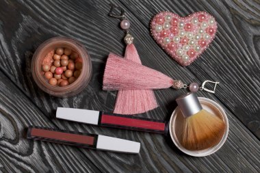 Kalp boncuklu broş. Küpeler pembe. Makyaj setinin yanında. Siyah beyaza boyanmış çam ağacından tahtalara.