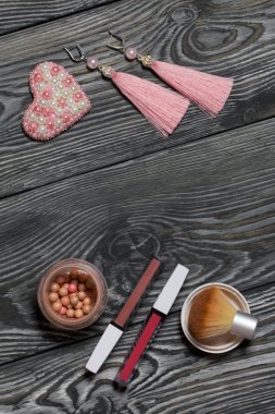 Kalp boncuklu broş. Küpeler pembe. Makyaj setinin yanında. Siyah beyaza boyanmış çam ağacından tahtalara.