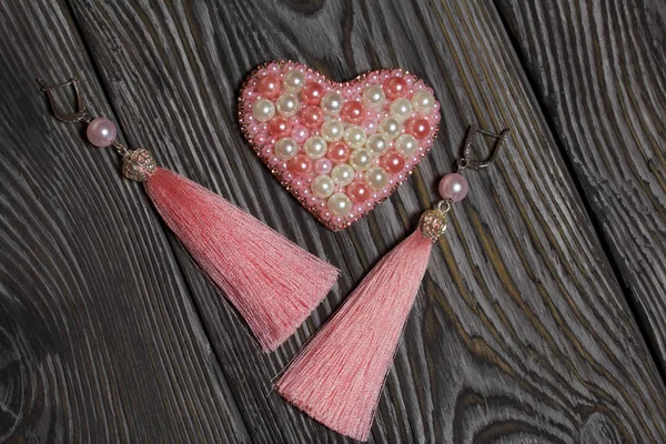 Broche de corazón. Pendientes borlas de color rosa. Sobre tablas de pino cepillado pintadas en blanco y negro . —  Fotos de Stock