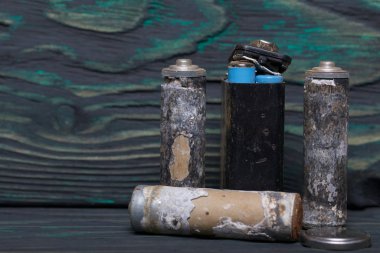 Aşınmayla kaplı kullanılmış piller. Siyah ve yeşile boyanmış çam ağaçlarının arka planında.