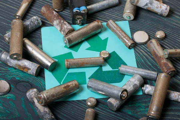 Baterias do tipo dedo usado revestidas com corrosão. Sinal de reciclagem de resíduos. Eles estão em placas de pinheiro escovado pintado em preto e verde . — Fotografia de Stock