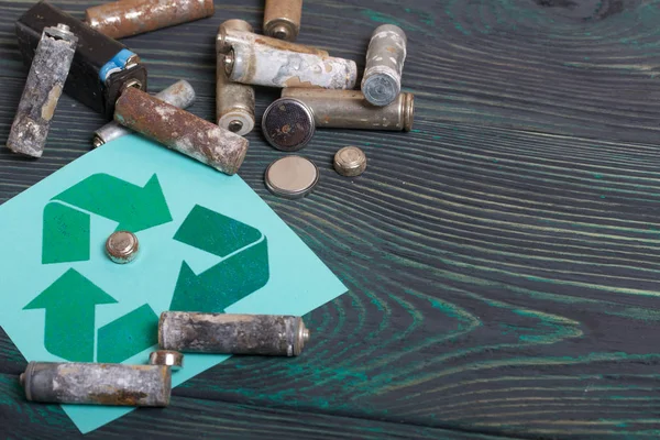 Batteries usagées de type doigt recouvertes de corrosion. Panneau recyclage des déchets. Ils reposent sur des planches de pin brossé peintes en noir et vert . — Photo