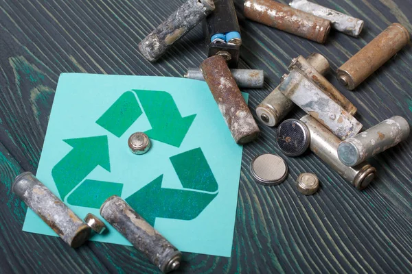 Baterias do tipo dedo usado revestidas com corrosão. Sinal de reciclagem de resíduos. Eles estão em placas de pinheiro escovado pintado em preto e verde . — Fotografia de Stock