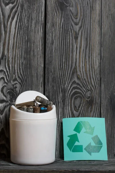 Waste bin. It contains finger-type batteries coated with corrosion. Nearby is a waste recycling sign. They lie on brushed pine boards painted in black and white. — Stock Photo, Image