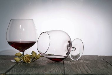 Kırmızı şaraplı bardaklar. Onlardan biri şarap kalıntılarıyla yan yatar. Kurumuş gül çiçekleri. Tahtaya çık. Arka planda çekilen.