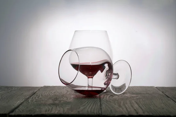 赤ワイングラス。そのうちの1つは、ワインの残りの部分とその側にあります。板の上に立つ。バックライトで撃たれた. — ストック写真