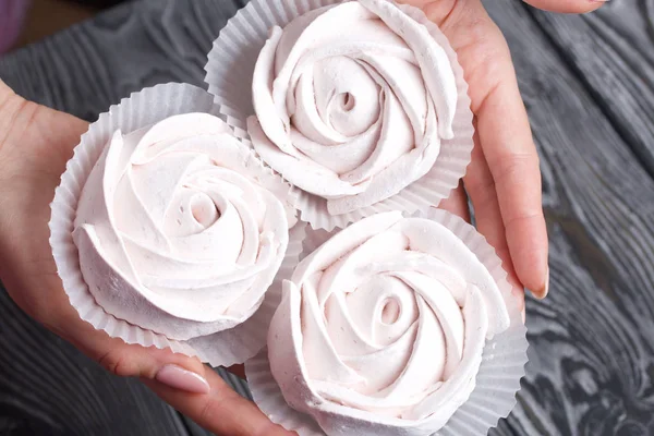 Marshmallows sotto forma di una rosa nei palmi di una donna. Sullo sfondo di tavole di pino spazzolato dipinte in bianco e nero . — Foto Stock