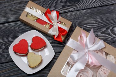 Kağıt ambalajda marşmelovlu sandviç. Fiyonka bağlanmış bir kurdeleyle bağlanmış. Yakınlarda kalp şeklinde lokum sandviçi var. Siyah ve beyaza boyanmış çam ağaçlarında.