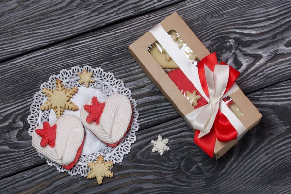 Marshmallow sandwich in paper craft packaging. Tied with a ribbon tied to a bow. Nearby are heart-shaped marshmallows sandwich and decorative snowflake cookies. On pine brushed boards painted in black