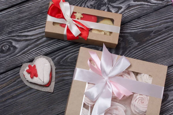 Marshmallow sandwich in paper craft packaging. Tied with a ribbon tied to a bow. Nearby are heart shaped marshmallows. On pine brushed boards painted in black and white. — 스톡 사진