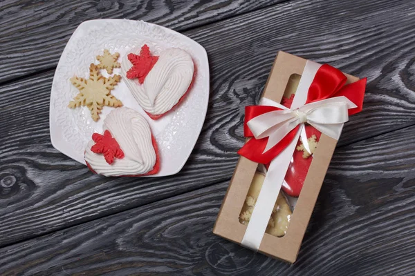 Marshmallow sandwich in paper craft packaging. Tied with a ribbon tied to a bow. Nearby are heart-shaped marshmallows sandwich. On pine brushed boards painted in black and white.