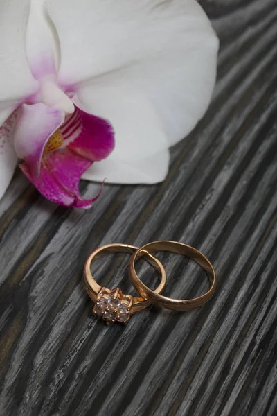 Evlilik yüzükleri ve orkide çiçeği. Siyah beyaza boyanmış çam ağacından tahtalara.