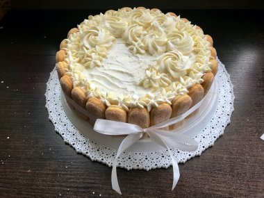 Savoiardi kurabiyeleri ile süslenmiş krem peynirli sünger kek. Yan tarafta, bir yay bağlı bir kurdele sarılmış.