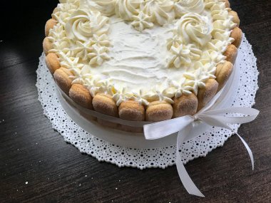 Savoiardi kurabiyeleri ile süslenmiş krem peynirli sünger kek. Yan tarafta, bir yay bağlı bir kurdele sarılmış.