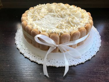 Savoiardi kurabiyeleri ile süslenmiş krem peynirli sünger kek. Yan tarafta, bir yay bağlı bir kurdele sarılmış.