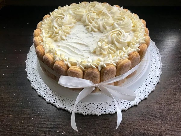 Pastel de esponja con queso crema, decorado con galletas Savoiardi. En el costado, envuelto en una cinta atada a un lazo . — Foto de Stock