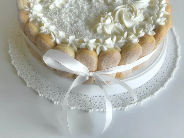 Gâteau éponge au fromage à la crème, décoré de biscuits Savoiardi. Sur le côté, enveloppé dans un ruban attaché à un arc . — Photo