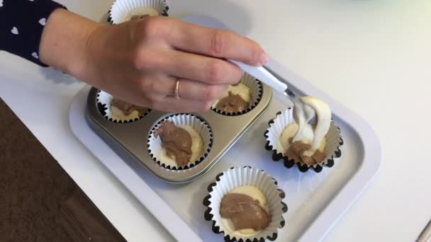 Eine Frau legt Teig mit und ohne Kakao in Muffinschalen. Herstellung eines Marmorkuchens. — Stockvideo