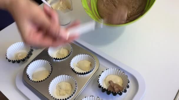 Uma mulher coloca massa com e sem cacau em pratos de bolos de muffin. A fazer um bolo de mármore. Vista de cima . — Vídeo de Stock