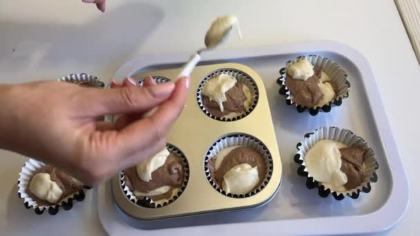 Een vrouw doet deeg met en zonder cacao in muffin bakschalen. Ik maak een marmeren taart. Close-up. — Stockvideo