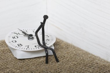 Figurines of man made from carpentry nails. They are sitting on the watch dial, one on the lap of the other. Symbol of love and the inexorable passage of time.