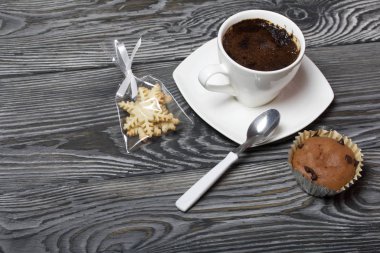 Beyaz fincanda kahve bir fincan tabağında duruyor. Yakınlarda bir kek ve çay tabağında bir kaşık var. Bir torba içinde, kar taneleri şeklinde kurabiyeler. Çam ağacından yapılmış tahtalarda.