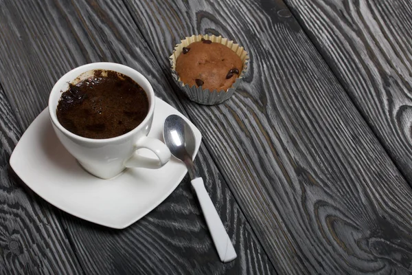 Káva v bílém šálku stojí na talíři. Nedaleko leží muffin a lžička na talíři. Na kartáčovaných borovicových deskách. — Stock fotografie