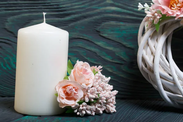 Big candle. Nearby lies a bouquet of artificial flowers. A part of the wreath of white painted vine is visible. Against the background of brushed boards painted in black and green. — Stock Photo, Image