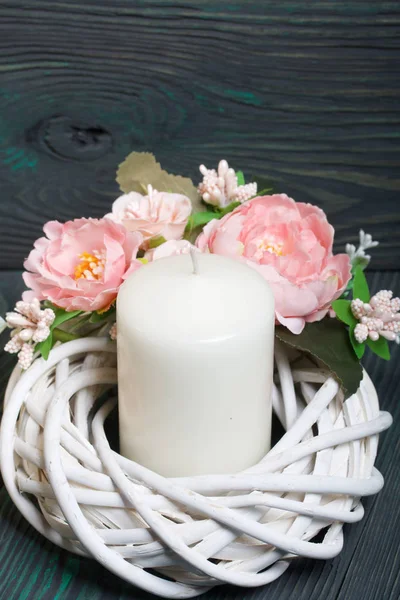 Decorative wreath of twigs of vines. Painted in white. Decorated with decorative flowers. There is a big candle in it. Against the background of brushed boards painted in black and green. — Stock Photo, Image