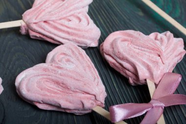 Çubukta kalp şeklinde narin pembe şekerlemeler. Bir tanesi kurdeleyle fiyonk bağlanmış. Siyah ve yeşile boyanmış çam ağaçlarının üzerinde yalanlar. Yakın plan..