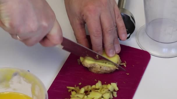 Un hombre corta trozos de jengibre en pedazos. Muy cerca se encuentra la miel en un recipiente y los elementos de la licuadora son visibles. Para cocinar jengibre con miel — Vídeos de Stock