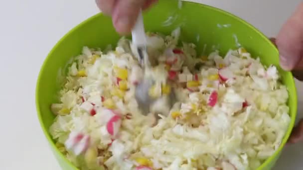 Un hombre hace una ensalada. Agregue un recipiente con palitos de cangrejo, maíz, col china y mayonesa. Termina de mezclar y deja una cuchara en la ensalada . — Vídeos de Stock