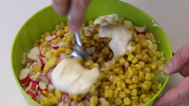 男がサラダを作る。彼はスプーンを取り、コンテナ内のみじん切りカニスティック、トウモロコシ、北京キャベツとマヨネーズを混合します。. — ストック動画