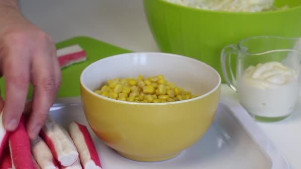 Un hombre hace una ensalada. Rebanadas de palitos de cangrejo en una tabla de cortar. En primer plano hay un recipiente con maíz y mayonesa. Primer plano de disparo . — Vídeo de stock