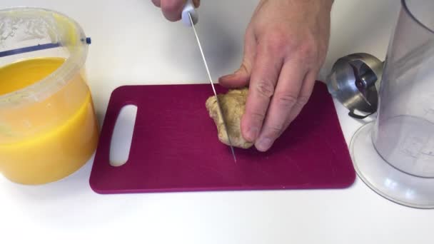 Un hombre toma un cuchillo y corta jengibre en rodajas. Muy cerca se encuentra la miel en un recipiente y los elementos de la licuadora son visibles. Para cocinar jengibre con miel . — Vídeos de Stock