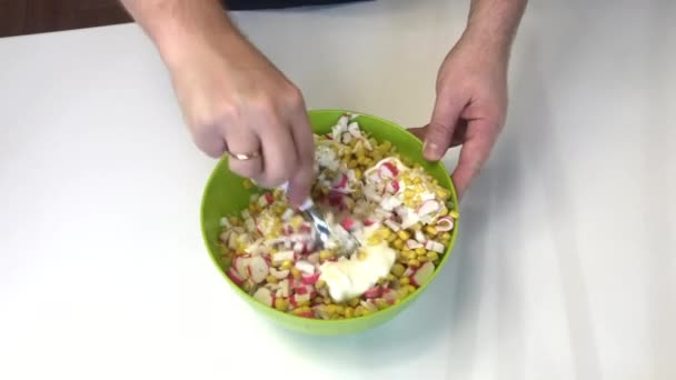 Um homem faz uma salada. Misturas paus de caranguejo picado, milho, repolho de Pequim e maionese em um recipiente . — Vídeo de Stock