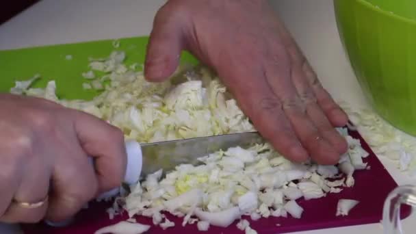 Um homem faz uma salada de couve de Pequim. Moagem repolho picado com uma faca em uma tábua de corte e joga-o em um recipiente. Imagem de close-up . — Vídeo de Stock