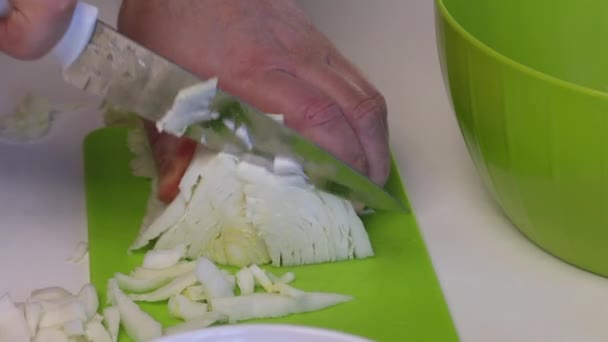 Человек делает салат из пекинской капусты. Нарезает капусту ножом на разделочной доске и бросает в контейнер. Рядом со столом есть и другие ингредиенты. Кукуруза, крабовые палочки и майонез. Close - — стоковое видео