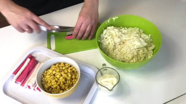 A man makes a salad. Slices crab sticks on a cutting board. Next to the container is shredded Beijing cabbage. Corn and mayonnaise are in containers. — Stock Footage A man makes a salad. Slices crab sticks on a cutting board. Next to the container is shredded Beijing cabbage. Corn and mayonnaise are in containers. Royalty Free Stock Video
