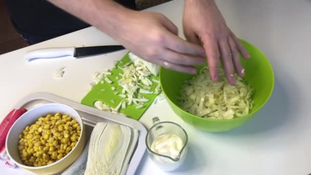 A man makes a salad of Beijing cabbage. Slices cabbage with a knife on a cutting board and throws it into a container. Next to the table are other ingredients. Corn, crab sticks and mayonnaise — Stock Footage A man makes a salad of Beijing cabbage. Slices cabbage with a knife on a cutting board and throws it into a container. Next to the table are other ingredients. Corn, crab sticks and mayonnaise Video Clip