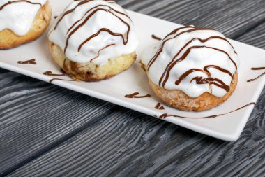 Çikolatayla süslenmiş, beyaz jöleli çörekler. Tabağa uzan. Fırçalanmış çam ağaçlarının arka planında.