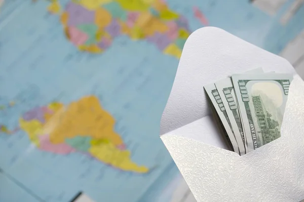 Yüz dolarlık banknotlar. Açık bir zarfın içine uzan. Bir dünya haritasının arka planına karşı. Üzerinde Güney Amerika ve Afrika 'nın siluetleri görünüyor..
