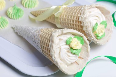 İki kremalı waffle konisi. Beyaz çikolata ve çikolata parçacıklarıyla süslenmişler. Onun yanında farklı renk ve şekillerde şekerlemeler var..