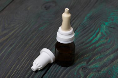 Burun damlası. Pipetli cam kavanoz. Kapağı çıkarılmış ve yakınlarda yatıyor. Fırçalanmış tahtaların arka planına karşı.