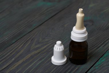 Burun damlası. Pipetli cam kavanoz. Kapağı çıkarılmış ve yakınlarda yatıyor. Fırçalanmış tahtaların arka planına karşı.