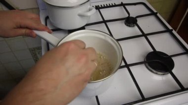 Elinde spatula olan bir adam, şekerleme yapmak için kaynar şurubu karıştırır. Gaz ocağındaki güveçte şurup..