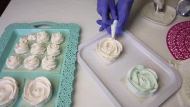 Bir tepside, gül şeklinde bir lokum ve klasik bir şekil oluşur. Pasta poşeti ve başlık kullanan bir kadın gül yaprakları şeklinde marşmelov yapar..