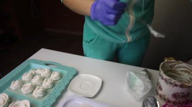 Bir kadın hamur torbasına şekerleme koyar ve masanın üzerine koyar. Tepsinin üzerinde dengelemek için bir lokum var..